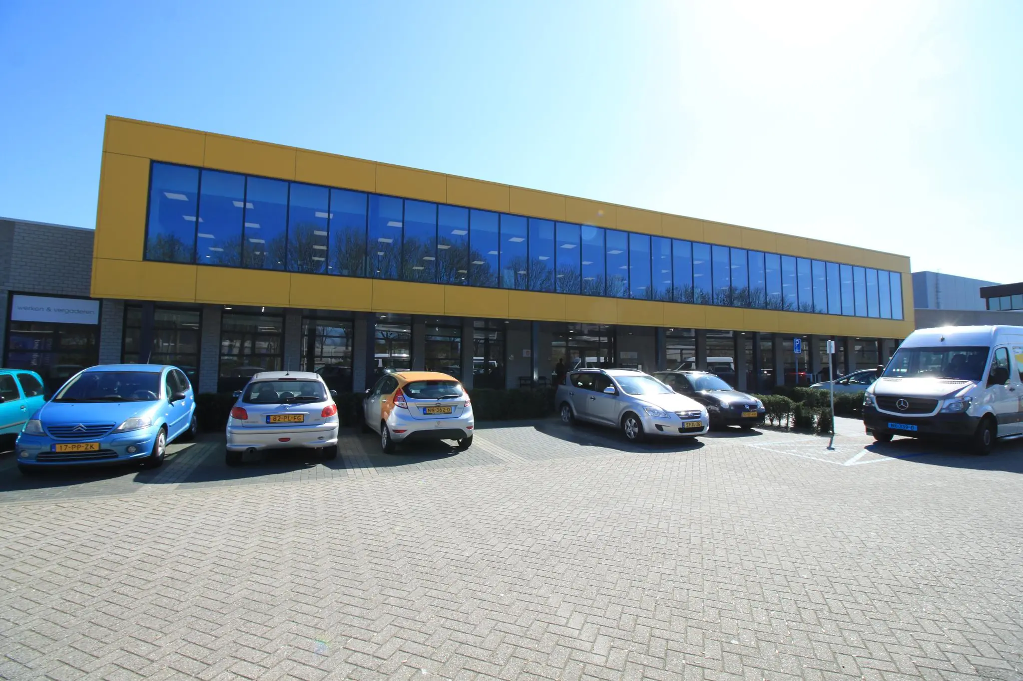 Modern bedrijfsgebouw aan de Niels Bohrweg met gele gevel en geparkeerde auto's op de voorgrond.